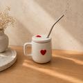 Handmade heart mug with ceramic lid and metal straw, hand-painted red heart on cream ceramic on a wooden table